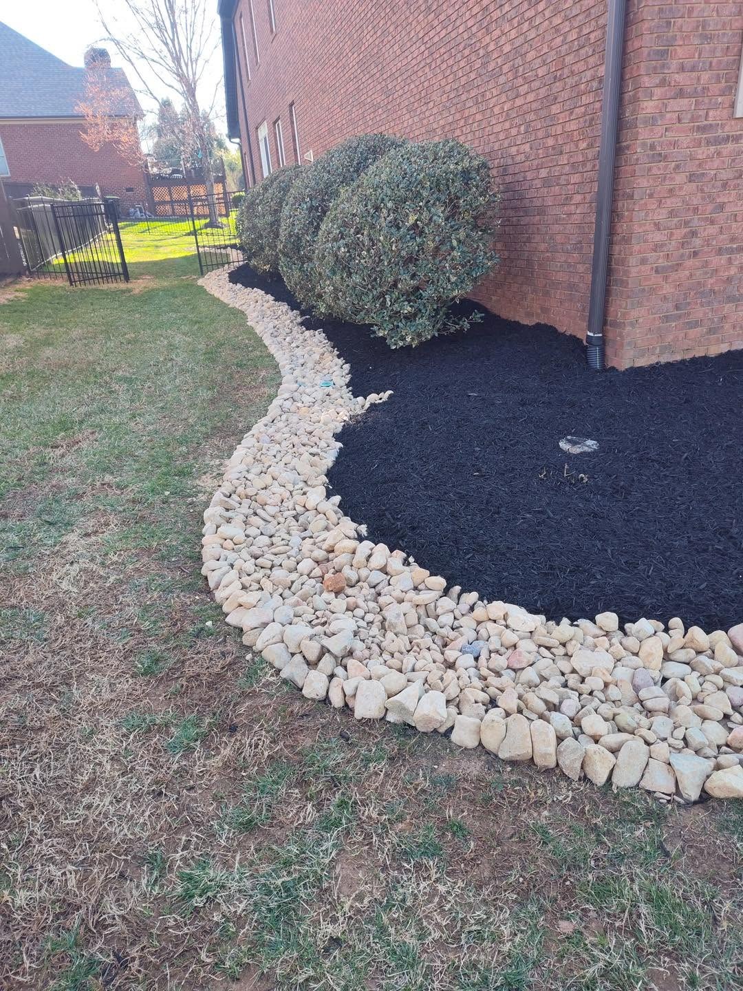 AAA Land Management landscaping photo showing a mulched bed with curved stone edging beside a brick home