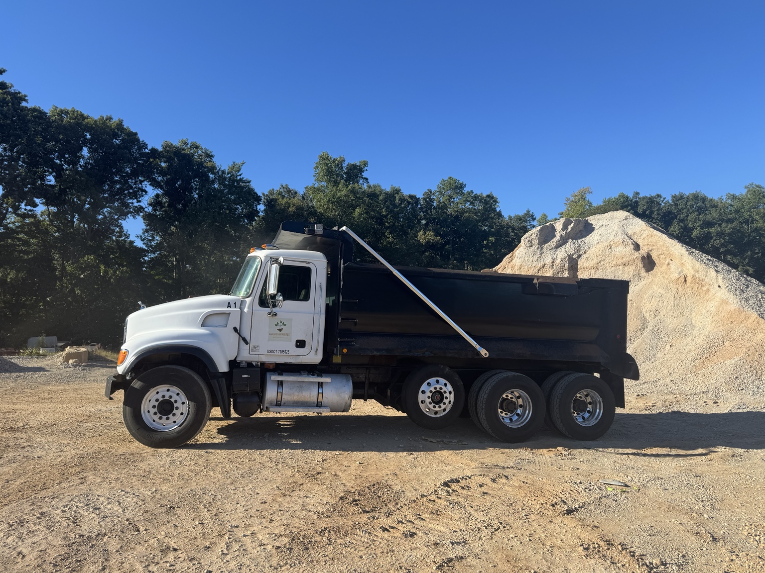 AAA Land Management's white tri-axle dump truck beside an aggregate stockpile